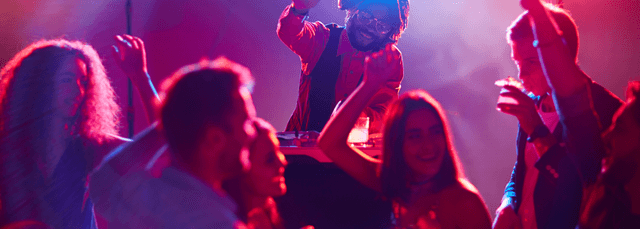 Live music performance with artist on stage and energized crowd with hands raised under vibrant purple and red stage lighting